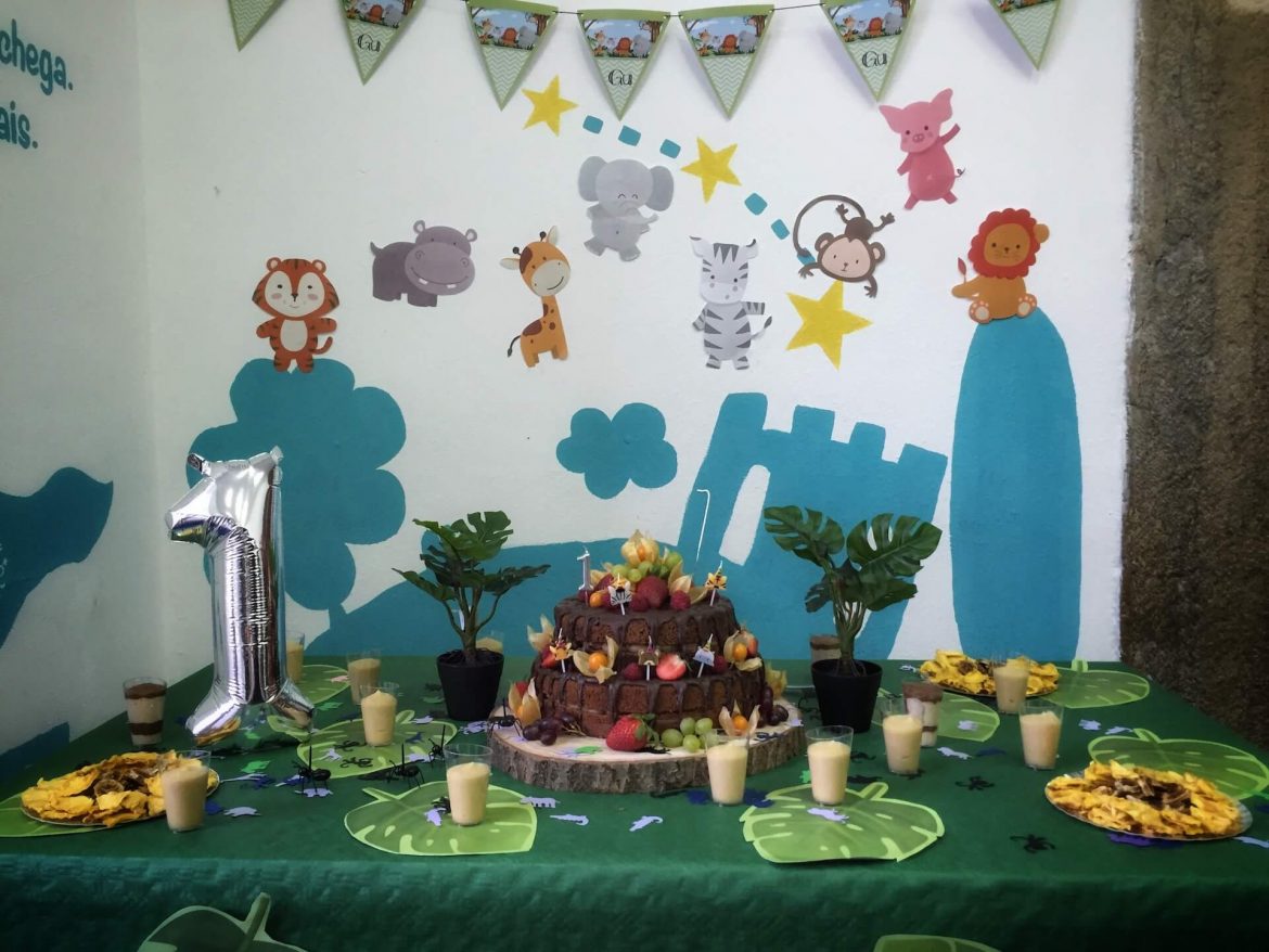 mesa com um bolo de anos vegan sem açucar, fruta desidratada e elementos decorativos da selva